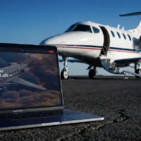 Eine Außenaufnahme auf einem asphaltierten Rollfeld bei sonnigem Wetter. Im Vordergrund steht ein geöffneter Laptop (MacBook Pro), auf dessen Bildschirm die Startseite der Finow Air Service Website mit dem Slogan „Ihr zuverlässiger Partner in der Luft – seit 1994“ zu sehen ist. Im Hintergrund parkt ein weißer Businessjet der Finow Air Service mit der Kennung D-IETB, dessen Passagiertür geöffnet ist. Die Szene kombiniert die digitale Präsenz des Unternehmens mit dem realen Flugbetrieb auf dem Flugplatz.